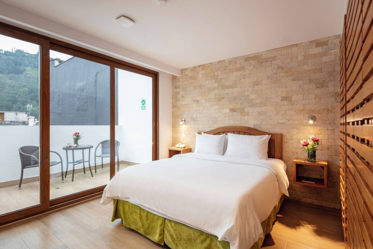 A bedroom with a large bed, a wooden headboard, a nightstand, and a small table with chairs.