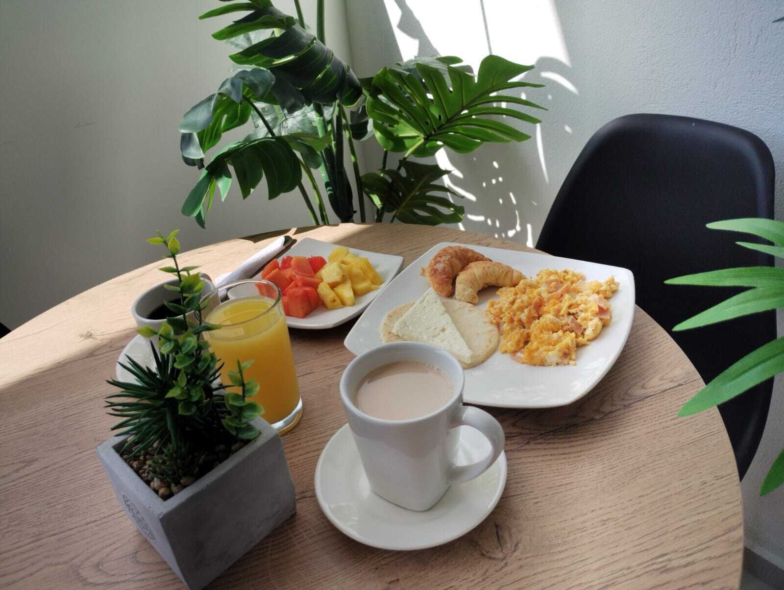 Een ontbijttafel met een bord roerei, toast, croissants en fruit, een glas sinaasappelsap en een kop koffie.
