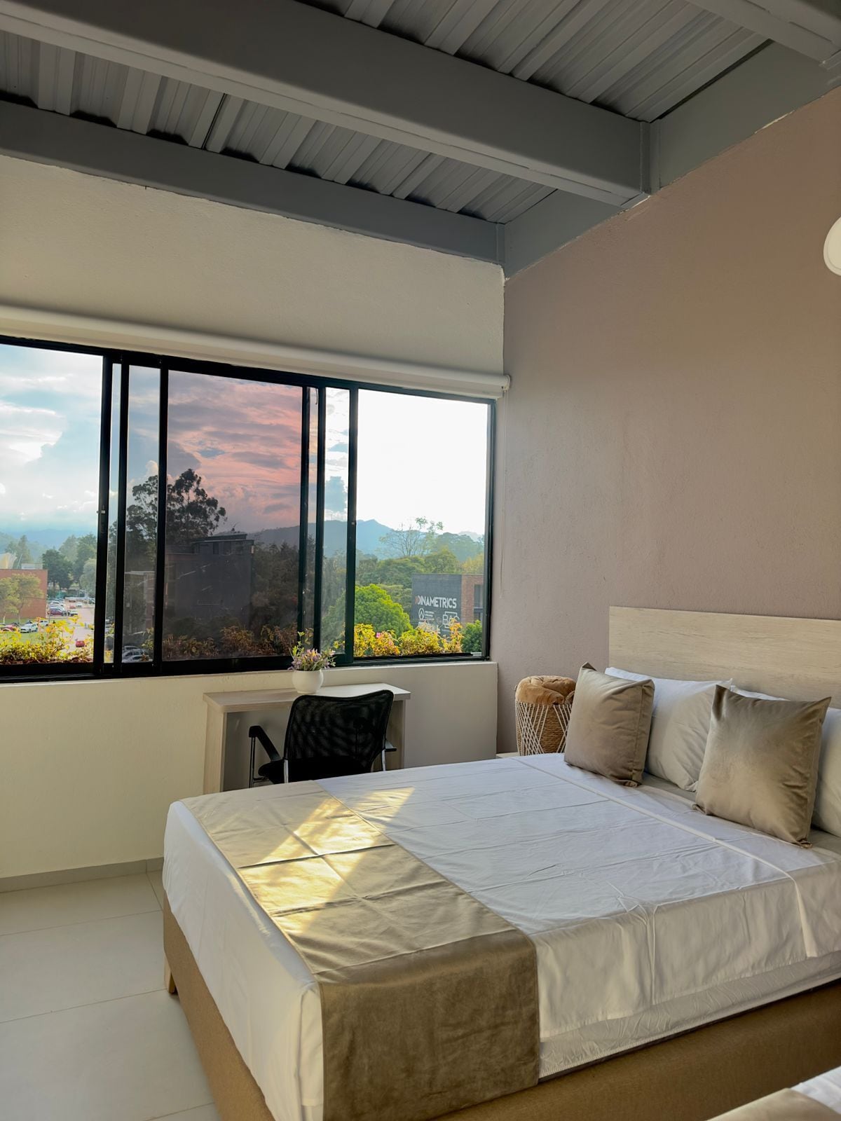 Um quarto com uma janela grande, uma cama, uma cadeira e uma mesa pequena.