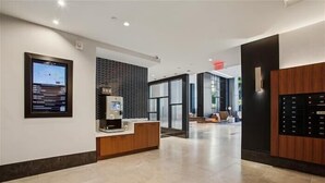 Un moderno vestíbulo de hotel con mostrador de recepción, máquina de café y pantalla digital.