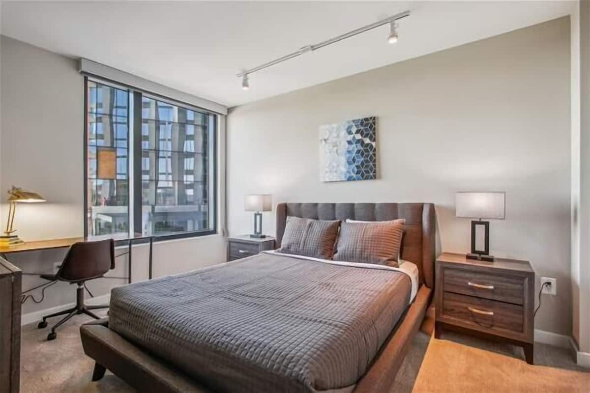 A modern bedroom with a large bed, a desk, and a window with a city view.