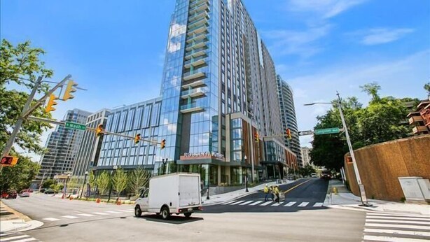 Un moderno edificio de gran altura con fachada de vidrio, situado en una intersección urbana.