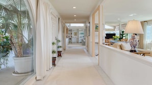A hallway with a view of a dining area, potted plants, and a large window with curtains. - Cove Watch by Avantstay A+ Views w/ Private Pool (La Jolla)
