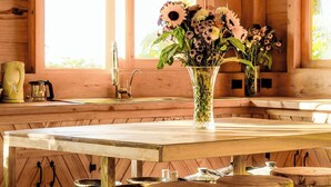 A rustic wooden cabin interior with a wooden table, chairs, and a vase of flowers.