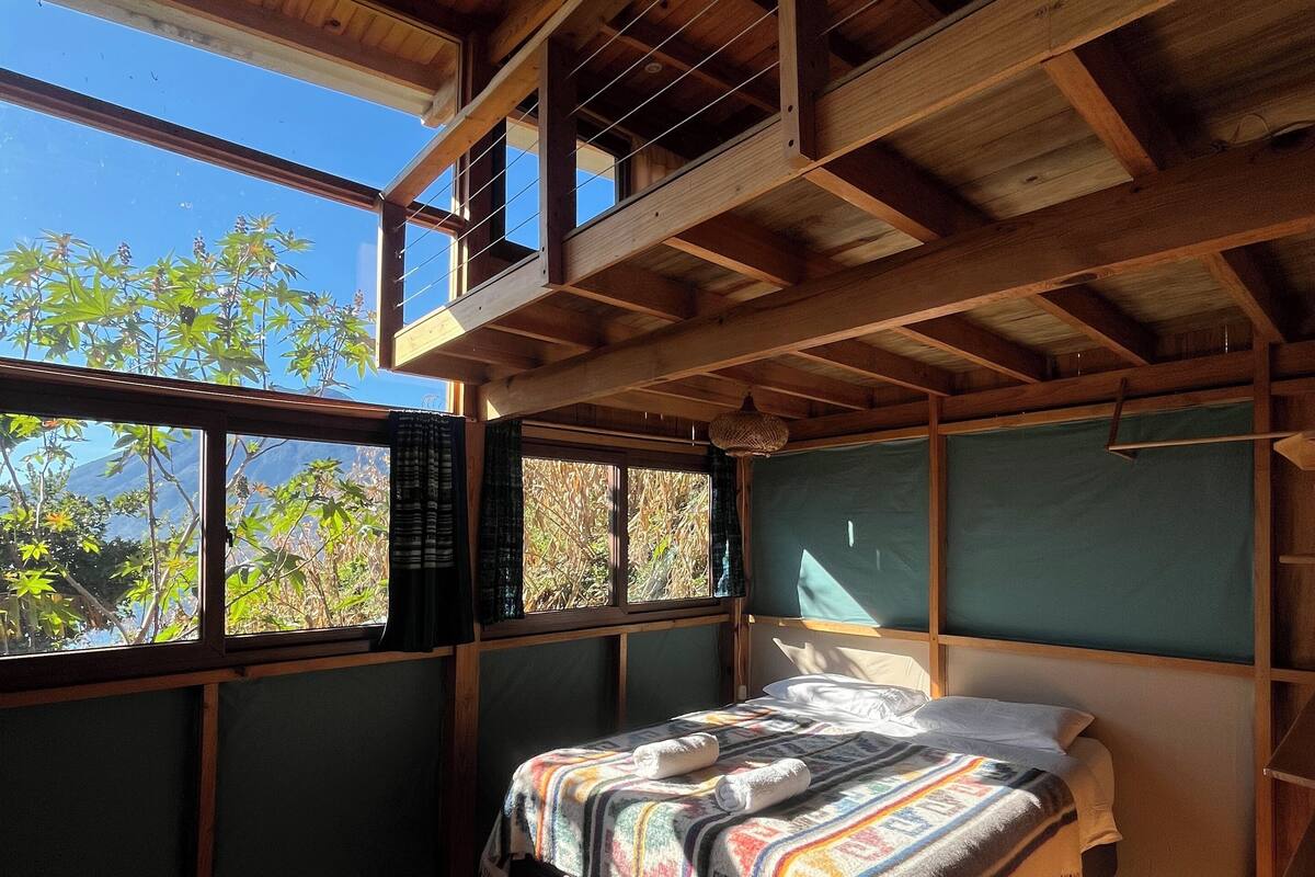A wooden room with a bed, a window, and a view of trees.