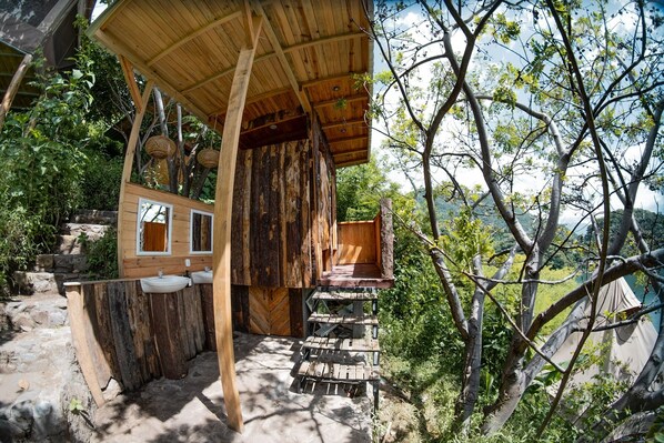 A rustic wooden cabin with a wooden deck, a small wooden structure with windows, and a view of a natural landscape.