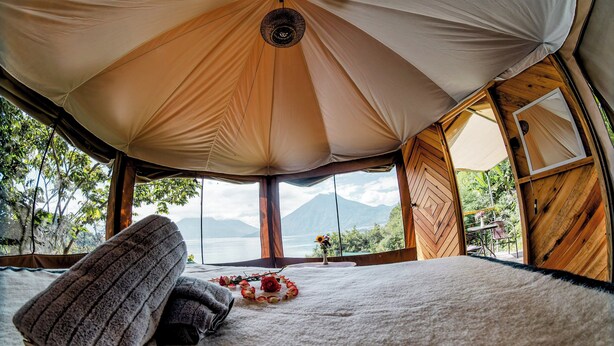 A cozy tent with a large window offering a view of mountains and a lake.