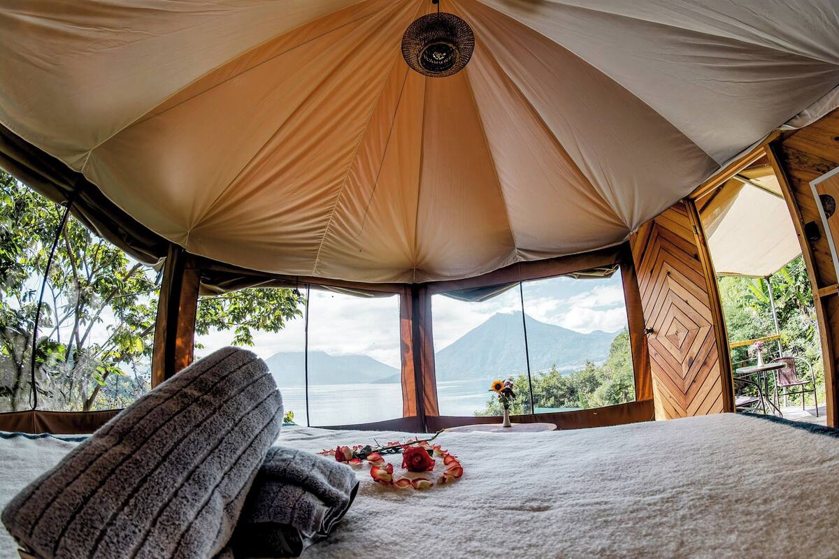 A cozy tent with a large window offering a view of mountains and a lake.