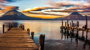 A wooden pier extending into calm waters with mountains in the background.