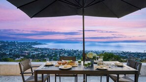 Une table dressée pour le petit-déjeuner, avec vue sur une ville côtière au coucher du soleil.