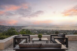 Une terrasse offrant une vue sur la ville et la côte, avec une table agrémentée d’une plante en pot et deux canapés.