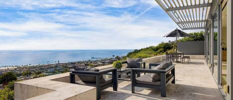 A patio with outdoor furniture, a pergola, and a view of the ocean.