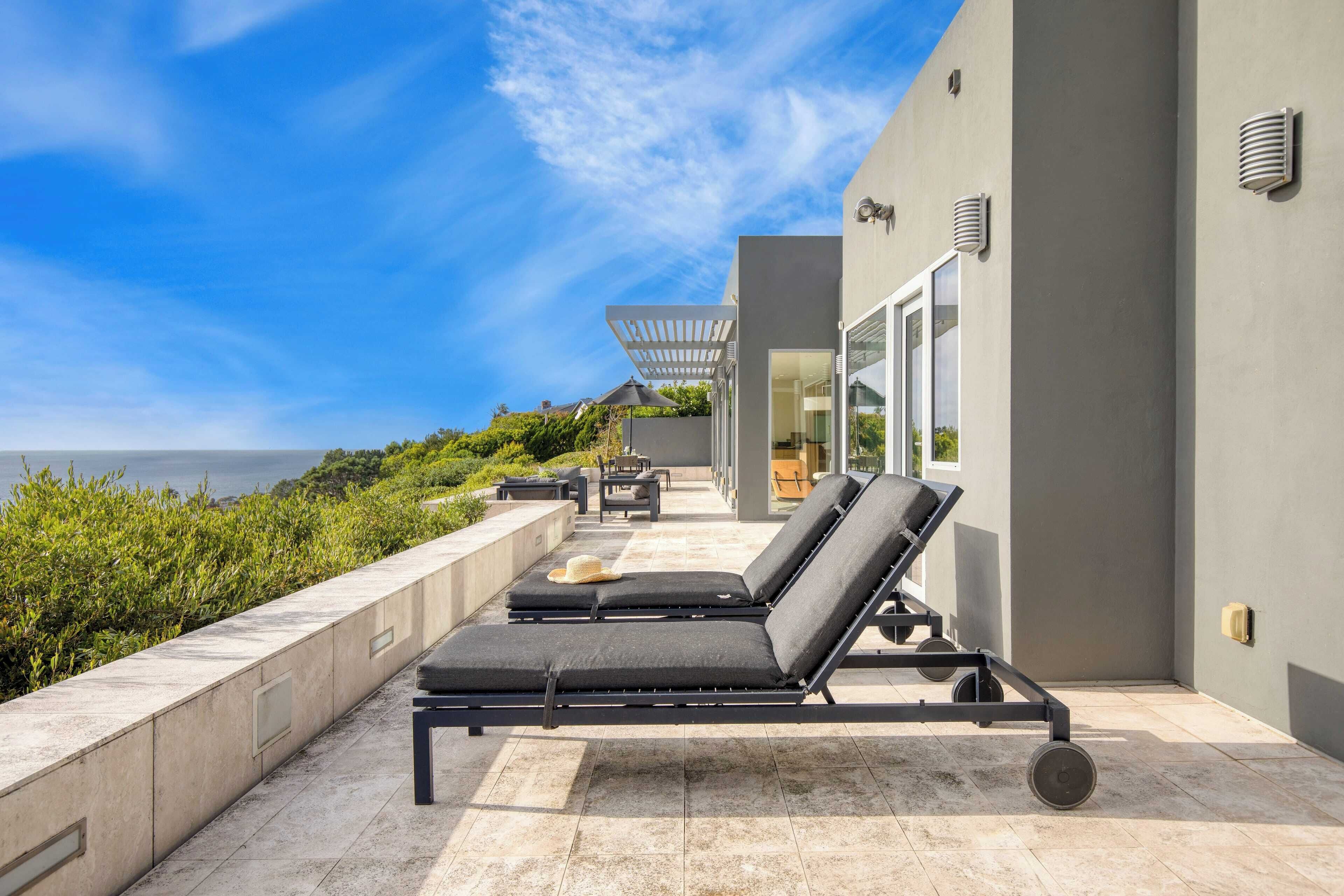 A modern outdoor lounge area with sun loungers and a view of the sea.