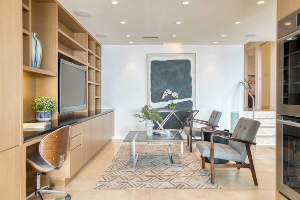 Una sala de estar moderna con una televisión de pantalla plana, estanterías de madera, una mesa de centro de vidrio y dos sillones grises.