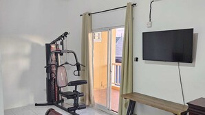 Une pièce avec un banc, un téléviseur, une fenêtre avec des rideaux et une porte donnant sur un balcon.