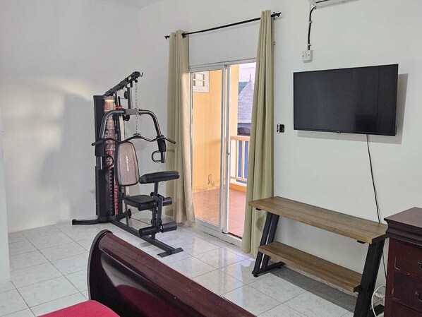 Une pièce avec un banc, un téléviseur, une fenêtre avec des rideaux et une porte donnant sur un balcon.