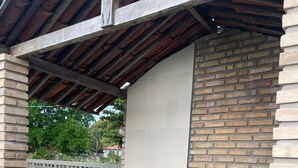 A covered outdoor barbecue area with a concrete floor, brick walls, and a metal grill. - Recanto Minduba (Japaratinga)