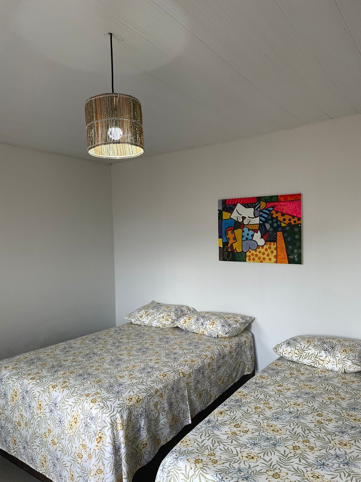 Un dormitorio con dos camas, una lámpara colgante y un cuadro abstracto y colorido en la pared.