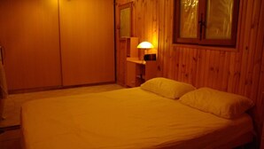 A bedroom with a bed, a nightstand, a lamp, and wooden walls. - Maison six Couchages à Proximité de la Mer. Location Aout, Septembre 2024 (Le Castellet)