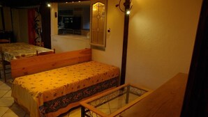 A small, cozy room with a single bed, a wooden bench, a glass table, and a window with a view of the kitchen. - Maison six Couchages à Proximité de la Mer. Location Aout, Septembre 2024 (Le Castellet)
