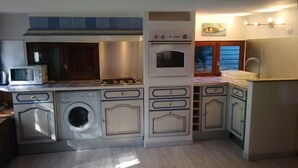 A compact kitchen with a microwave, stove, oven, and built-in washing machine. - Maison six Couchages à Proximité de la Mer. Location Aout, Septembre 2024 (Le Castellet)