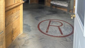 Una habitació amb una porta de fusta, una banca, un quadre de cavalls i un símbol de la lletra 'P' al terra.