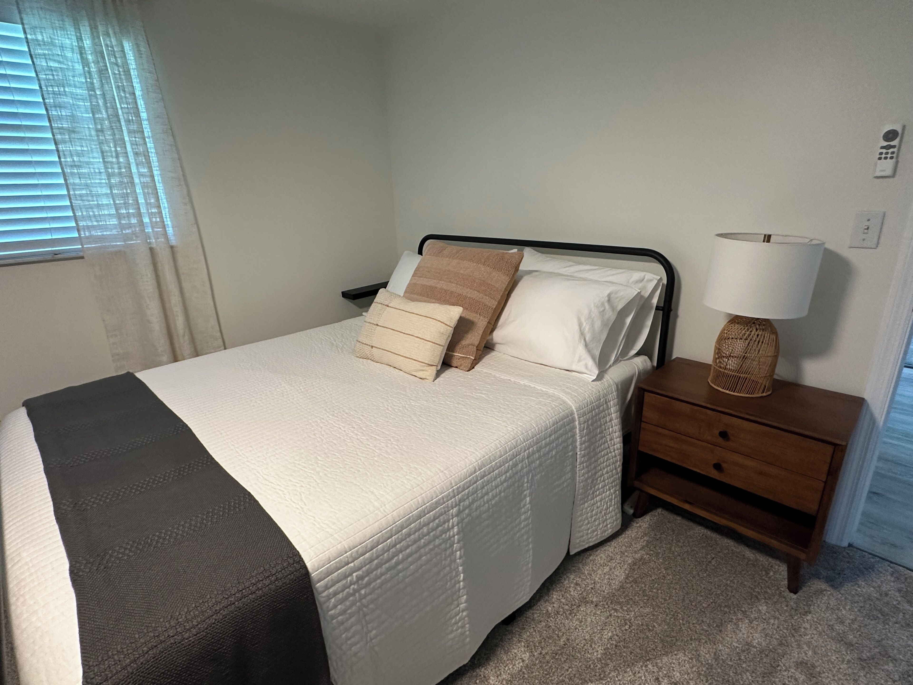 Een net opgemaakt bed met een wit en donker dekbed, een bedlamp en een houten nachtkastje.