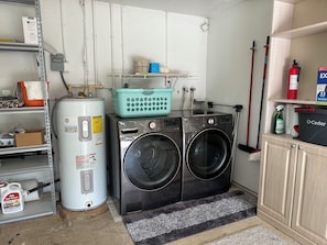 Un espace buanderie comprenant un lave-linge, un chauffe-eau et une étagère avec des produits de nettoyage.