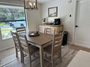 A dining area with a wooden table and chairs, a coffee maker, and a window with blinds.