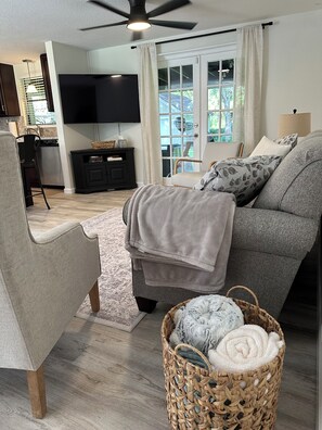 A living room with a sofa, a chair, a TV, a dining area, and a view of the outdoors.