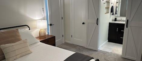 A bedroom with a bed, bedside table, lamp, and a sliding closet door leading to a bathroom.