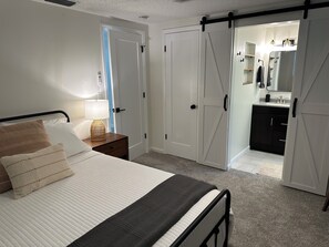 A bedroom with a bed, bedside table, lamp, and a sliding closet door leading to a bathroom.