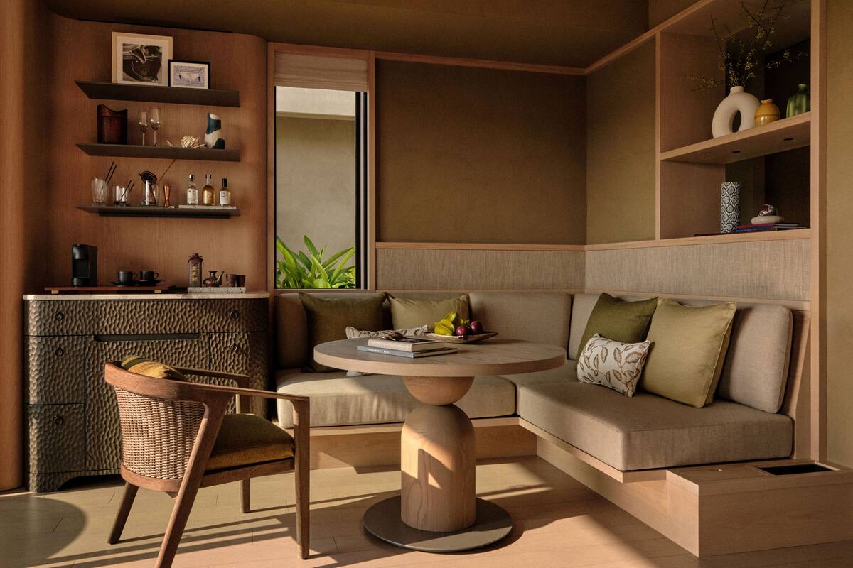 Una sala moderna con un sofá, una mesa redonda de centro y una silla de mimbre. Hay estanterías con objetos decorativos y un armario con utensilios de cocina.