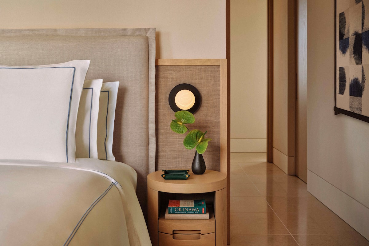 Un dormitorio ordenado con cama, mesita de noche y una obra de arte enmarcada en la pared.