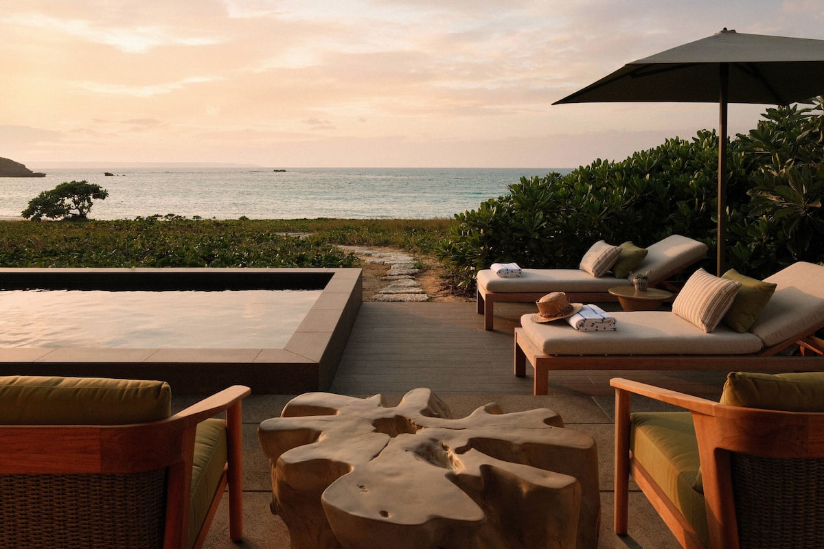 Un espacio al aire libre iluminado por el sol con piscina, sillones de descanso y vistas al mar.