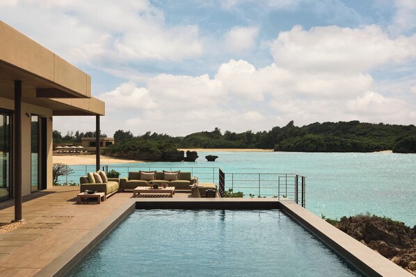 Zona junto a la piscina con mobiliario exterior y vistas al mar.