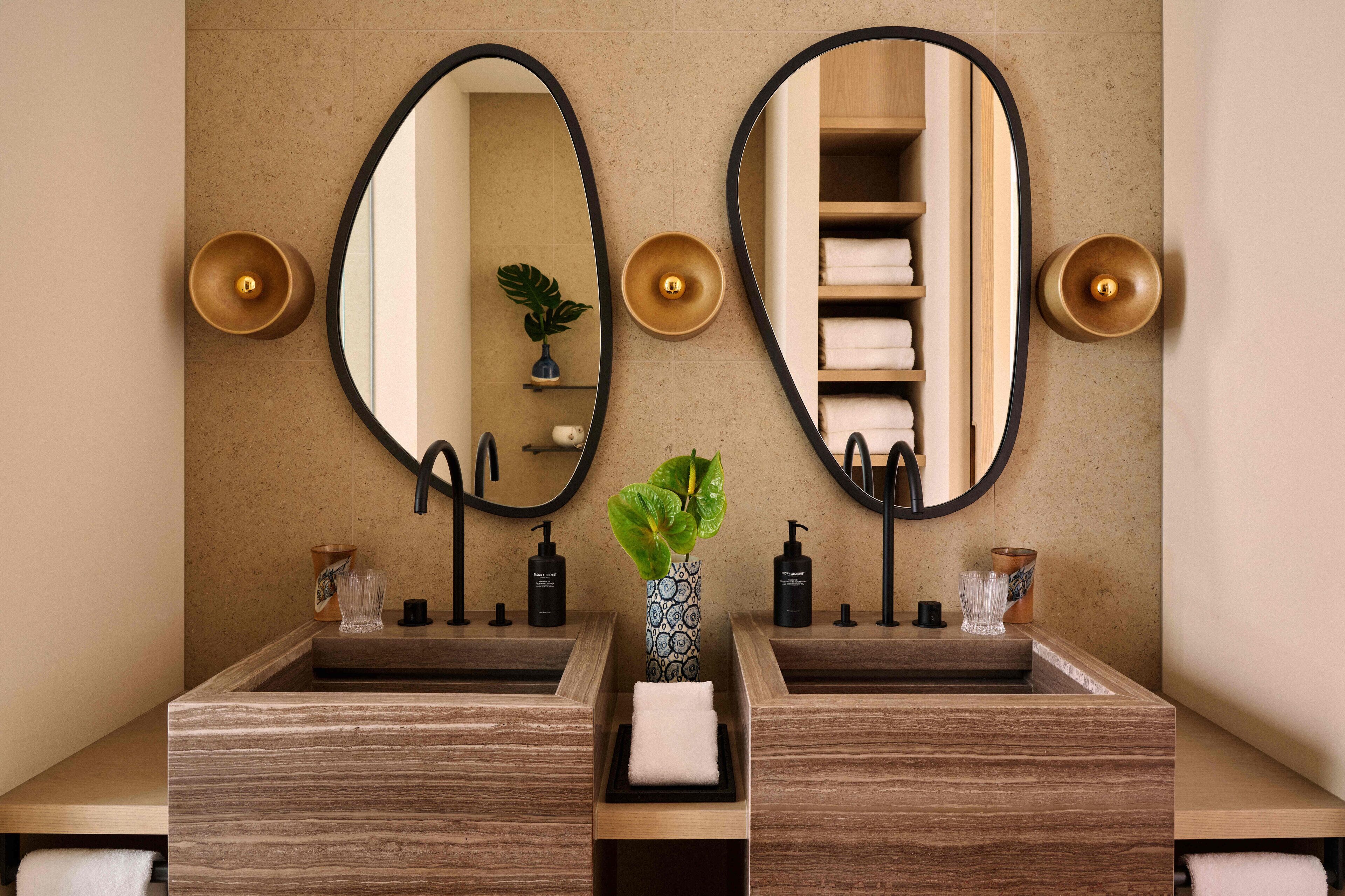 A bathroom with two sinks, a mirror, and a vase with a plant.