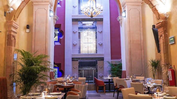 A dining area with tables set for a meal, a chandelier, and a view of the lobby. - Casa Postal Hotel Boutique (Querétaro)
