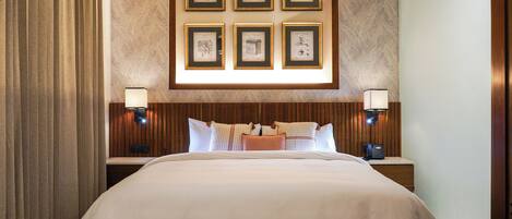 A hotel room with a large bed, two bedside tables with lamps, a headboard with framed artwork, and a window with curtains.