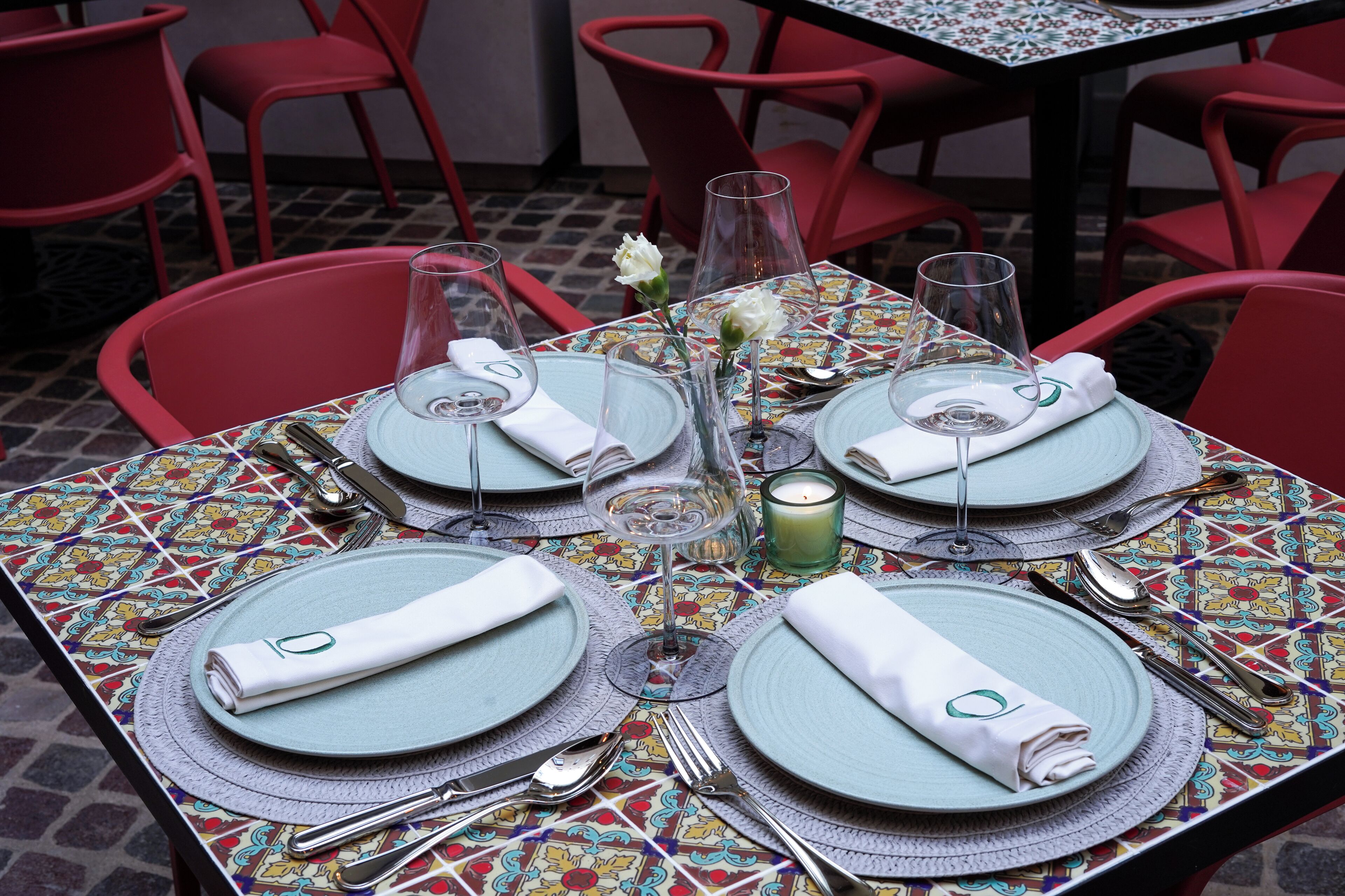 A table set for four with red chairs, a patterned tablecloth, and a candle centerpiece.