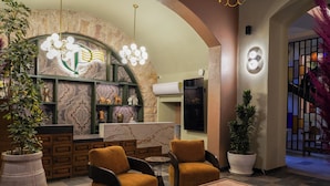 A lobby with a stone archway, a reception desk, two armchairs, a coffee table with books, and potted plants. - Casa Postal Hotel Boutique (Querétaro)