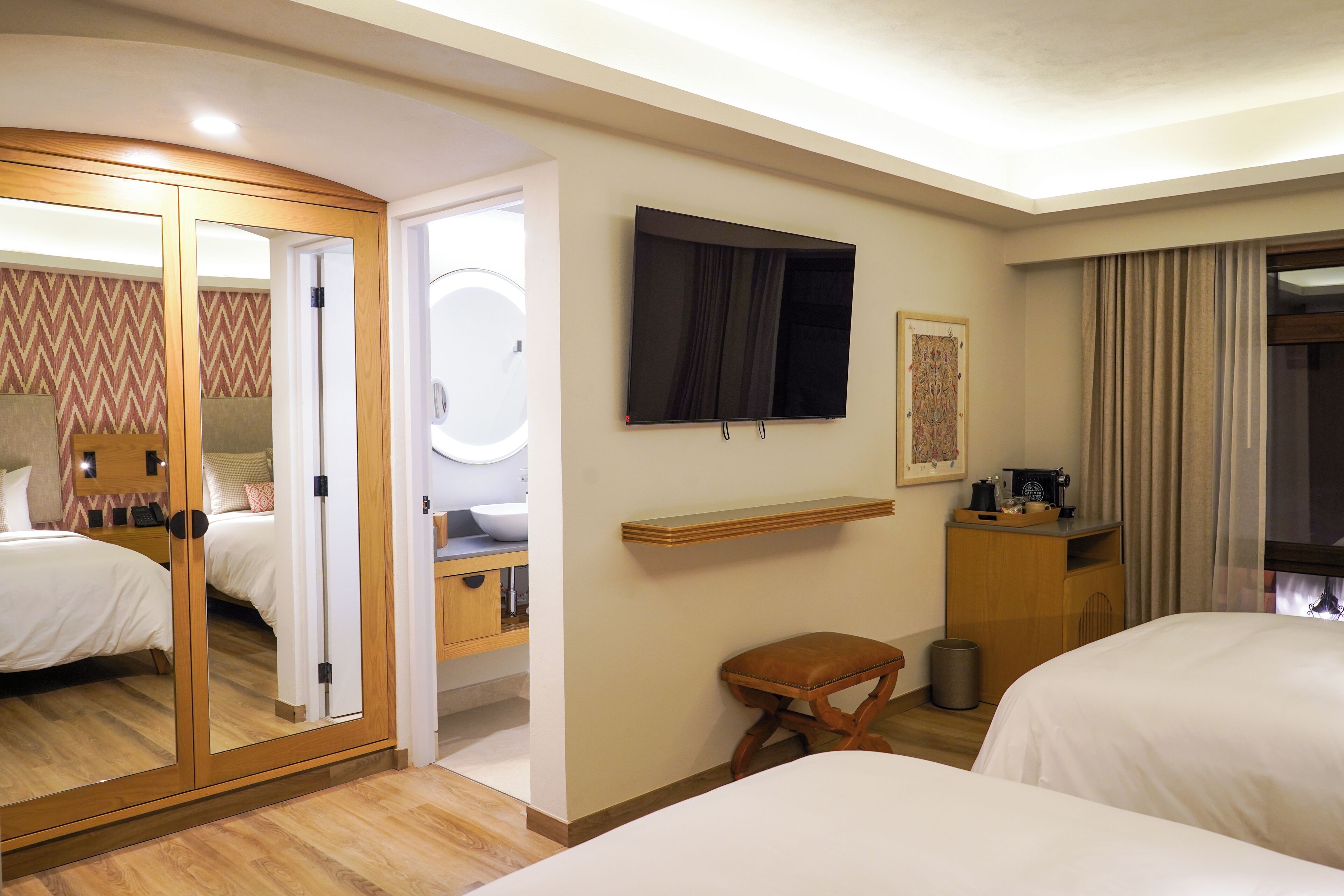 Habitación de hotel con dos camas, un espejo, televisor, una mesita y un escritorio con silla.