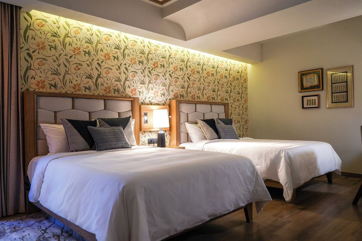 A hotel room with two beds, a floral wallpaper, and framed pictures on the wall.