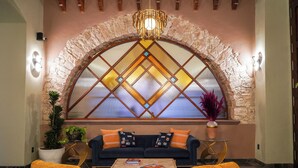 A lobby with a stone arch, a dark blue sofa with orange cushions, a coffee table, and two armchairs with yellow cushions. - Casa Postal Hotel Boutique (Querétaro)