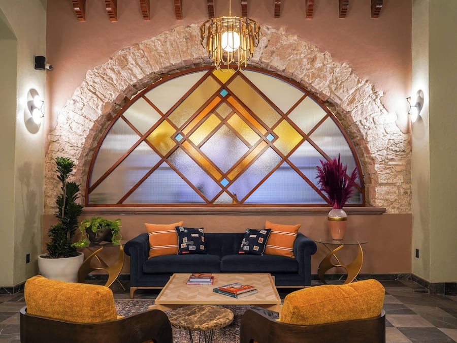 Un hall con un arco de piedra, un sofá azul oscuro con cojines naranjas, una mesa de centro y dos sillones con cojines amarillos.