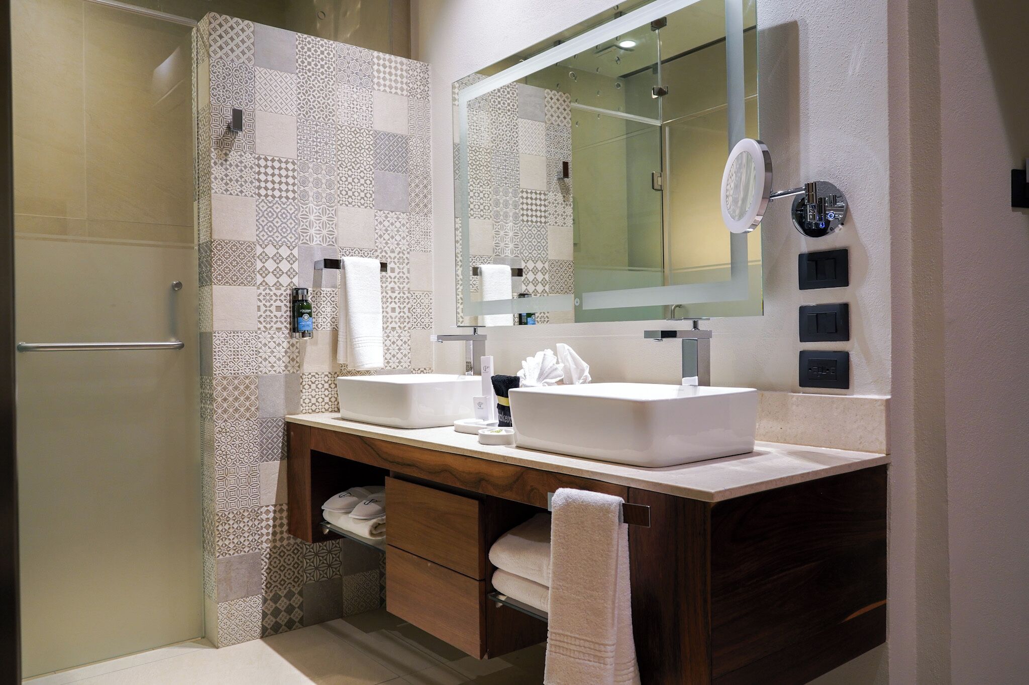 A modern bathroom with two sinks, a large mirror, and a shower area.