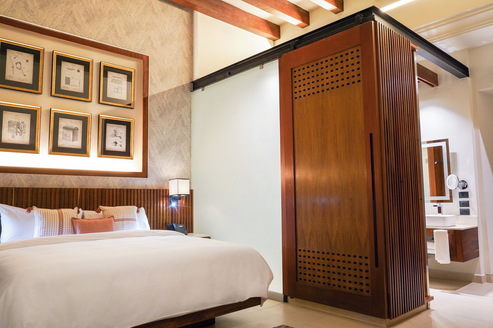 Habitación de hotel con una cama grande, un armario de madera, una estantería con marcos y un baño a la vista al fondo.
