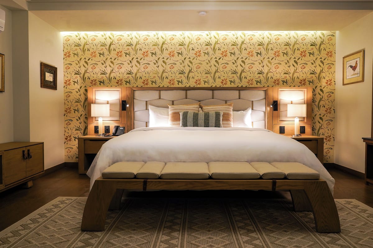 A large bed with a headboard, two bedside lamps, and a patterned wallpaper.