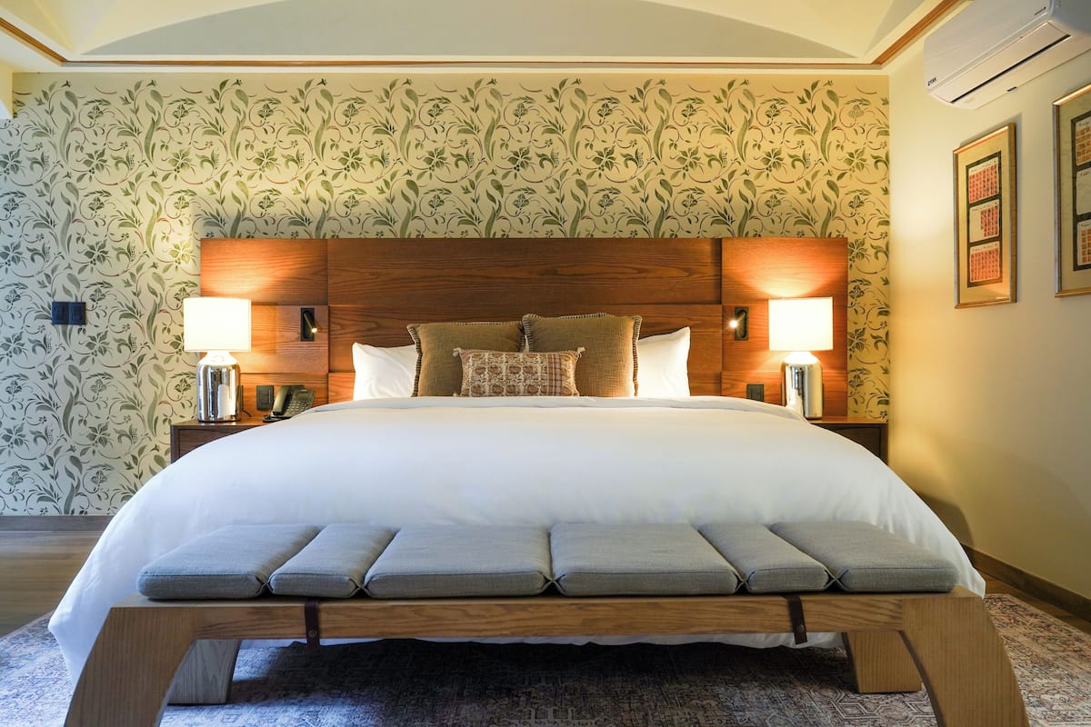 A neatly made bed with a wooden headboard, two bedside lamps, and a bench at the foot of the bed.