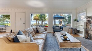 A living room with a leather sofa, a coffee table, and a view of the outdoors. - West Shore Lake House by Avantstay Ski Cabin w/ Backyard Sledding Hill! (Homewood)